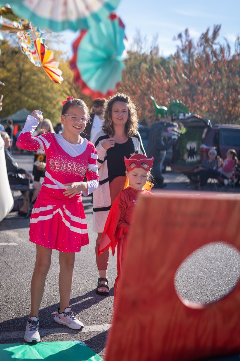 32 family-friendly Halloween events in Birmingham 3 Girl in cheerleader costume and child in superhero mask and cape at a trunk-or-treat event, with decorated cars and paper decorations nearby