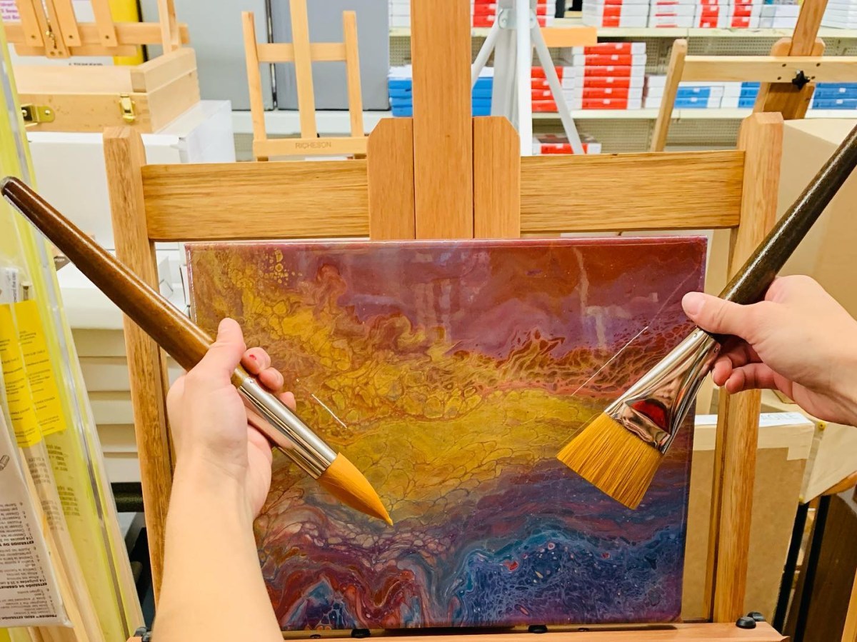 Hands holding brushes near artwork