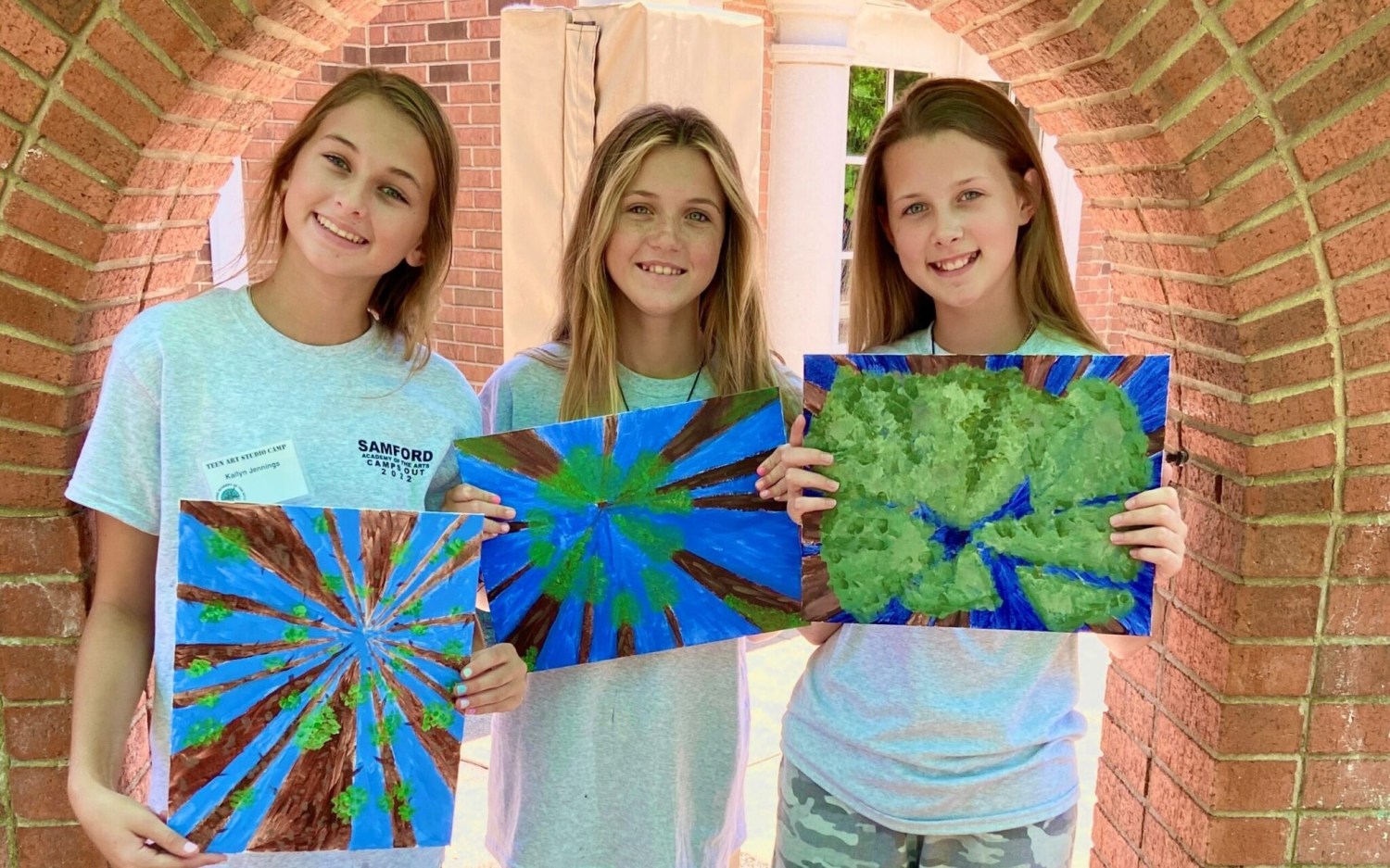 Three girls holding colorful paintings.