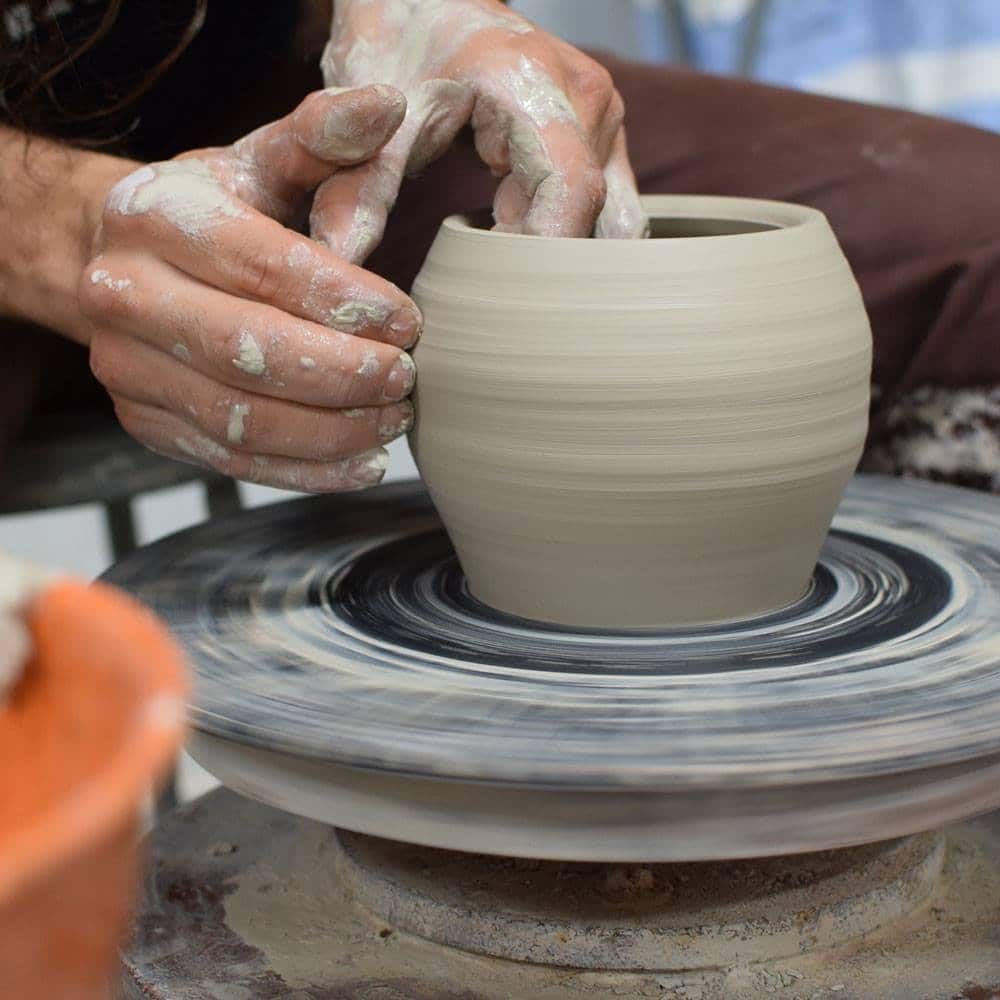 Hands shaping clay on pottery wheel