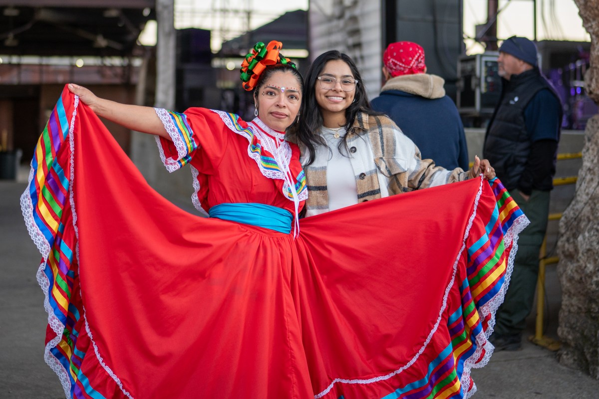 6 ways to celebrate Día de los Muertos in Birmingham 2 Woman in traditional red Mexican dress with rainbow ribbon trim poses with a smiling attendee at Día de los Muertos in Birmingham