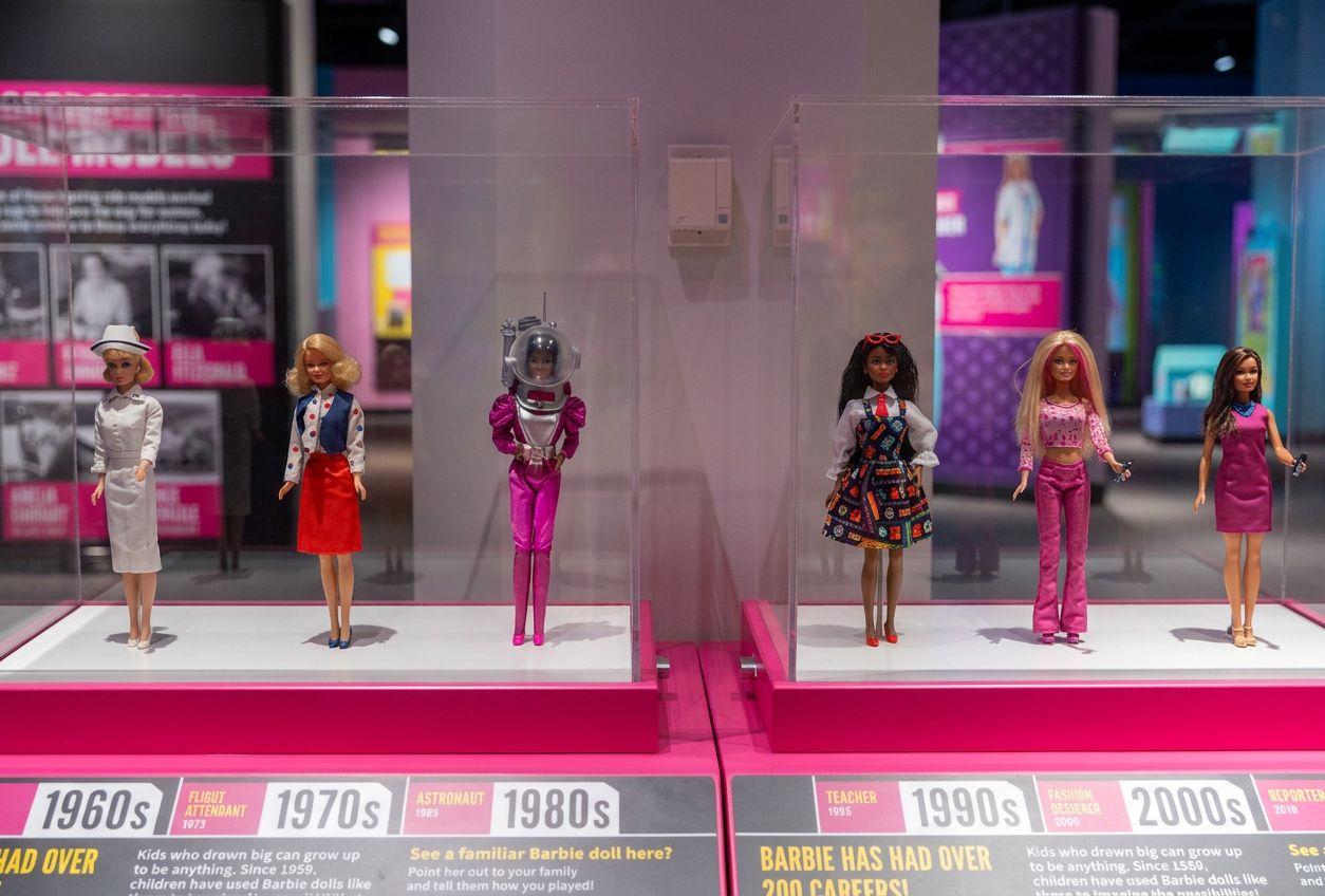 Display case of career Barbie™ dolls from the 1960s–2000s, including astronaut, teacher and reporter outfits