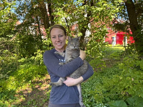 A smiling woman holds a striped gray cat outdoors.
